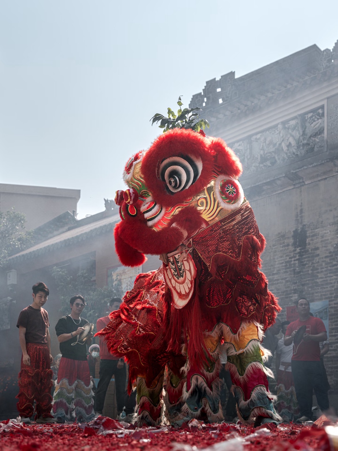 岭南醒狮在传统祠堂前表演,地面铺满爆竹碎屑,烟雾弥漫